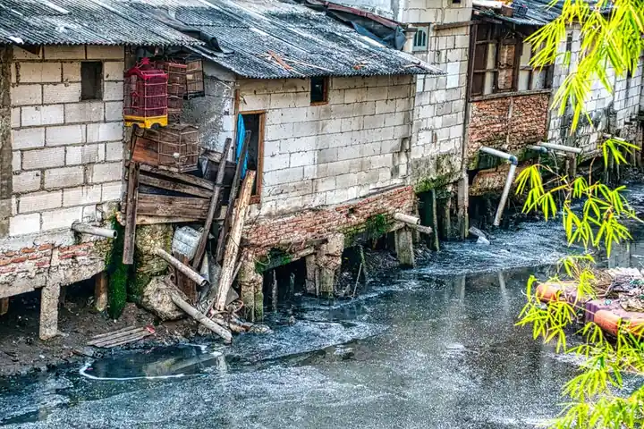 Polluted river beside rundown houses in Jakarta's slum, illustrating urban poverty and environmental issues.